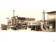 Black and white photograph of old fashioned cars parked in front of businesses