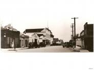 Black and white photograph of old fashioned cars parked in front of businesses