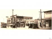 Black and white image of old fashioned cars parked in front of businesses